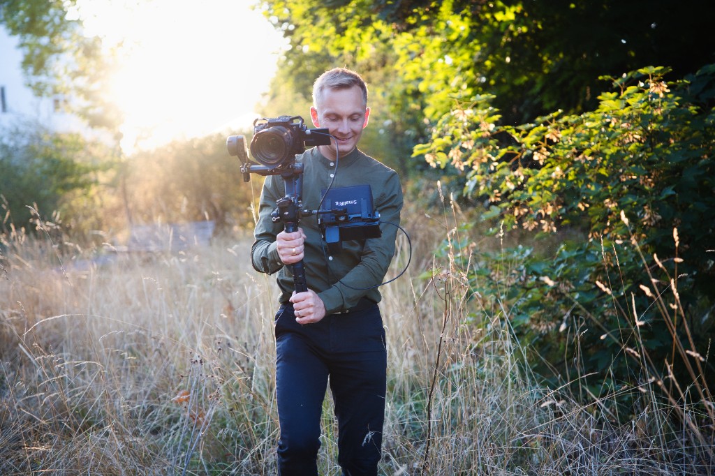 Jeremias Forell mit Gimbal und Monitor im Gegenlicht auf einer Wiese