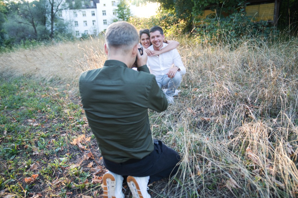 Jeremias Forell kniet im Gras und fotografiert ein Paar