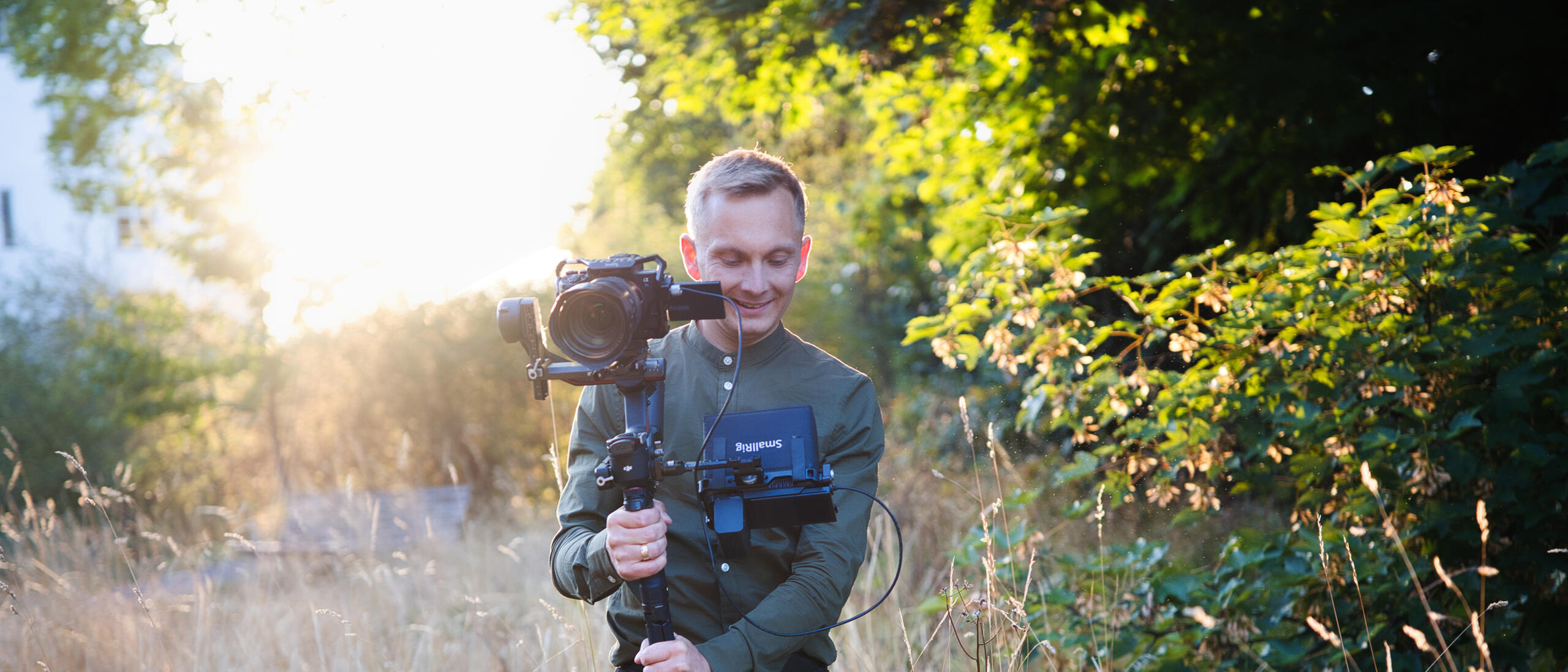 Jeremias Forell mit Gimbal und Monitor im Gegenlicht auf einer Wiese